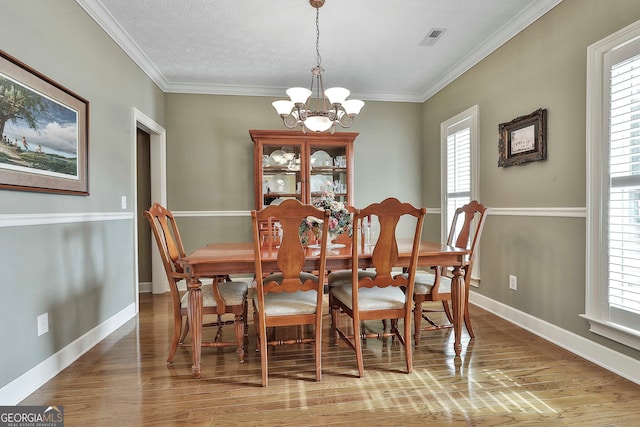 dining area featuring hardwood / wood-style floors, a wealth of natural light, an inviting chandelier, and crown molding