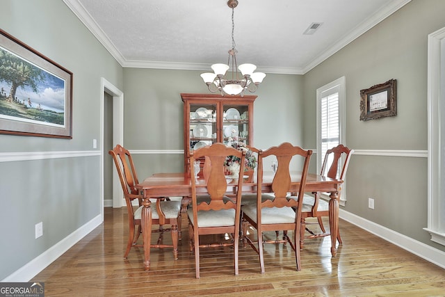 dining area featuring visible vents, a notable chandelier, ornamental molding, wood finished floors, and baseboards