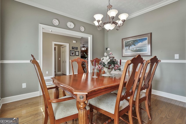 dining area with ornamental molding, ceiling fan with notable chandelier, wood-type flooring, and a textured ceiling