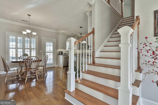 staircase featuring visible vents, a notable chandelier, ornamental molding, hardwood / wood-style flooring, and a textured ceiling