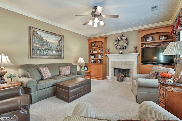 living room with ceiling fan, a tiled fireplace, crown molding, and carpet floors