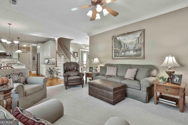 living room featuring ceiling fan with notable chandelier, a textured ceiling, light wood-type flooring, and ornamental molding