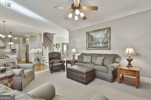 living area featuring visible vents, baseboards, stairs, ornamental molding, and ceiling fan with notable chandelier