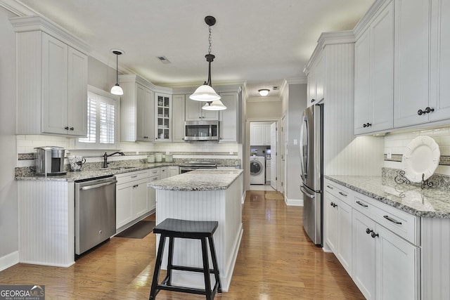 kitchen with visible vents, washer / clothes dryer, stainless steel appliances, dark wood-type flooring, and a center island