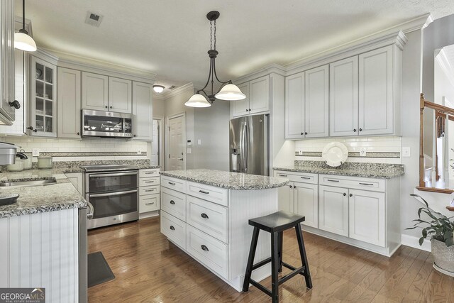 kitchen with crown molding, stainless steel appliances, white cabinetry, decorative light fixtures, and sink