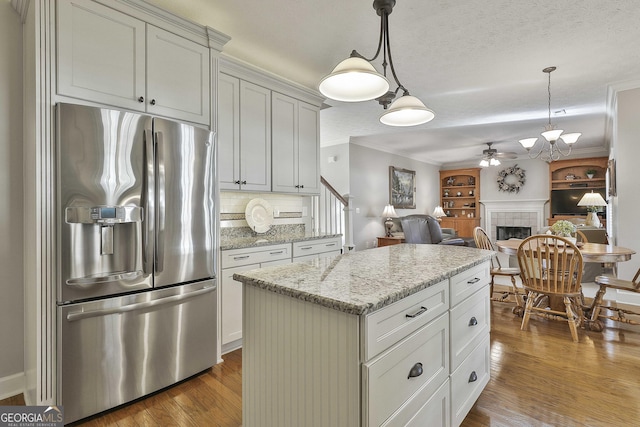 kitchen featuring wood finished floors, a ceiling fan, a fireplace, stainless steel fridge with ice dispenser, and ornamental molding