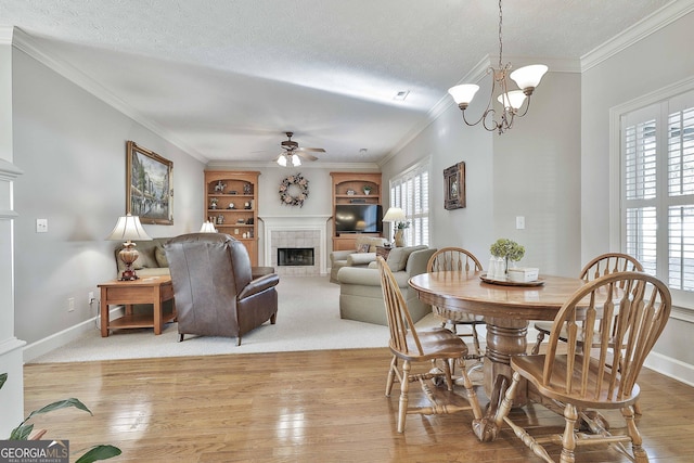 dining room featuring baseboards, a tiled fireplace, light wood-type flooring, ceiling fan with notable chandelier, and a textured ceiling