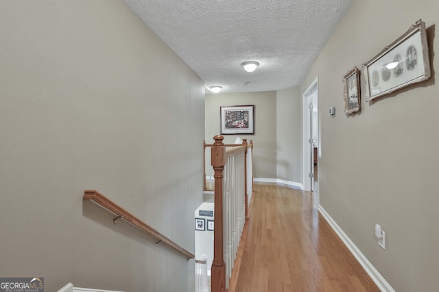 hallway with a textured ceiling, an upstairs landing, baseboards, and light wood-type flooring