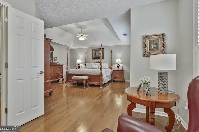 bedroom with light wood-type flooring, visible vents, a raised ceiling, a textured ceiling, and baseboards