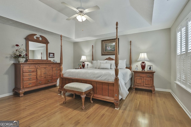 bedroom with baseboards, a raised ceiling, light wood-style floors, and a ceiling fan