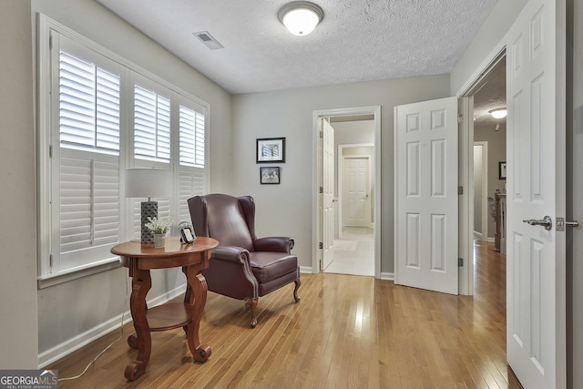 living area featuring visible vents, light wood-style flooring, a textured ceiling, and baseboards