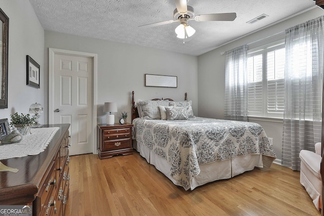 bedroom featuring ceiling fan, visible vents, a textured ceiling, and light wood-style flooring