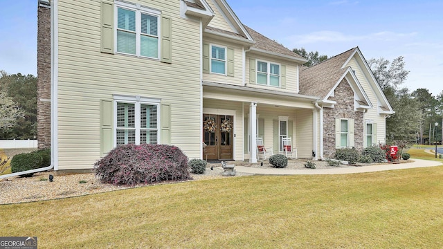 view of front of property featuring stone siding, covered porch, a front lawn, and a shingled roof