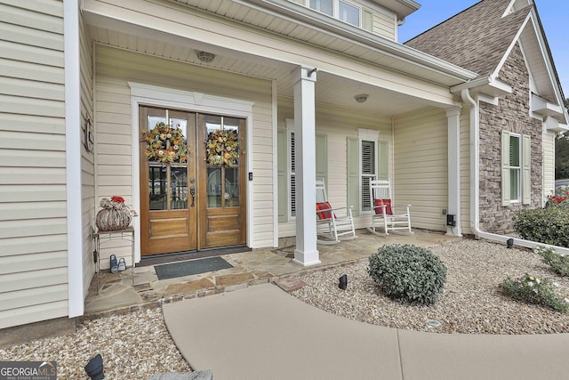 property entrance with french doors, covered porch, stone siding, and roof with shingles