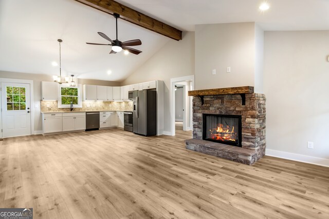 unfurnished living room featuring a stone fireplace, ceiling fan with notable chandelier, sink, beam ceiling, and light hardwood / wood-style flooring