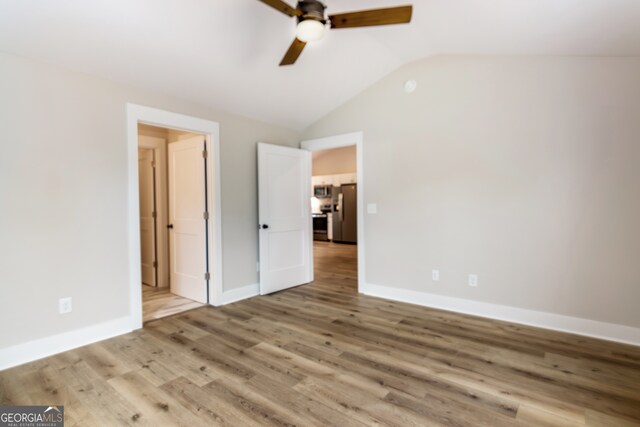 unfurnished bedroom featuring hardwood / wood-style floors, lofted ceiling, ceiling fan, and stainless steel refrigerator with ice dispenser