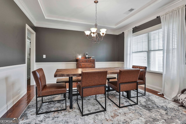 dining area with ornamental molding, a raised ceiling, hardwood / wood-style flooring, and a chandelier