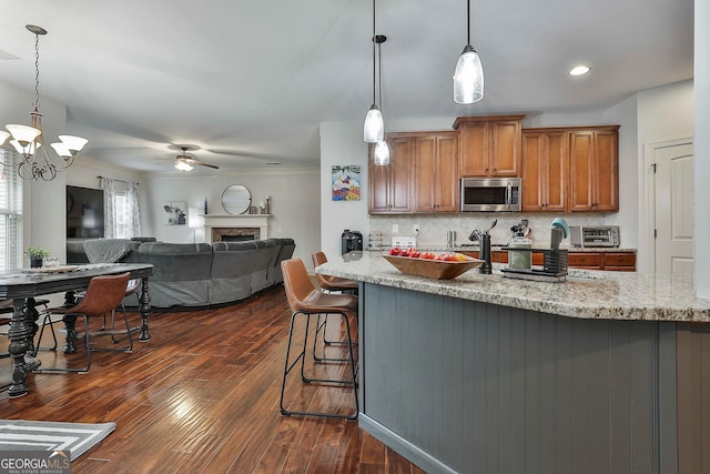 kitchen with light stone counters, tasteful backsplash, a breakfast bar area, dark wood-type flooring, and pendant lighting