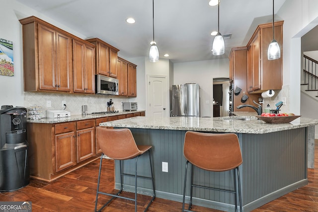 kitchen featuring stainless steel appliances, hanging light fixtures, dark hardwood / wood-style floors, and light stone counters