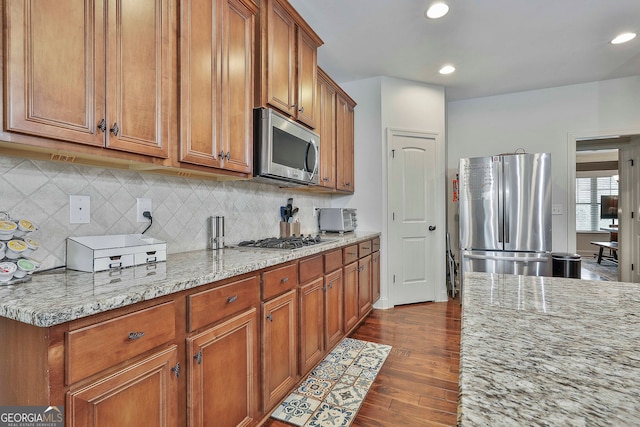 kitchen featuring light stone countertops, decorative backsplash, appliances with stainless steel finishes, and dark hardwood / wood-style flooring