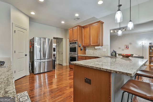 kitchen featuring appliances with stainless steel finishes, dark hardwood / wood-style flooring, pendant lighting, light stone countertops, and kitchen peninsula