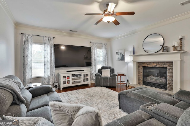 living room featuring a stone fireplace, dark wood-type flooring, ornamental molding, and ceiling fan