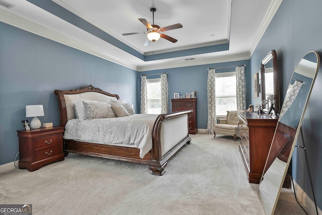 carpeted bedroom with a tray ceiling, ornamental molding, multiple windows, and ceiling fan