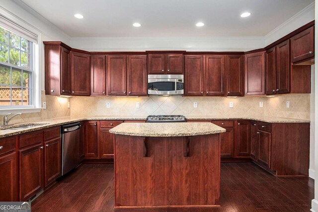 kitchen featuring stainless steel appliances, dark wood-type flooring, crown molding, sink, and a center island