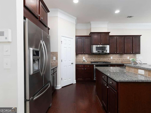 kitchen featuring stainless steel appliances, dark wood-type flooring, dark stone counters, decorative backsplash, and ornamental molding