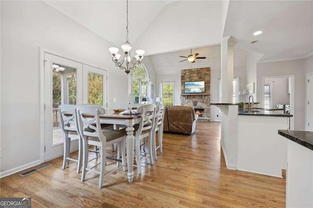 dining area with high vaulted ceiling, ceiling fan with notable chandelier, sink, light wood-type flooring, and a fireplace