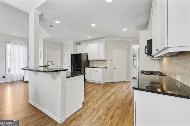 kitchen featuring black appliances, light wood-type flooring, white cabinetry, and dark stone countertops