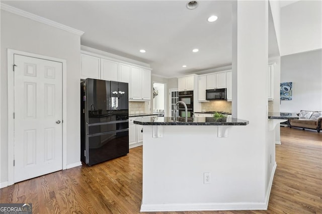 kitchen with backsplash, black appliances, light wood-type flooring, a kitchen bar, and white cabinetry