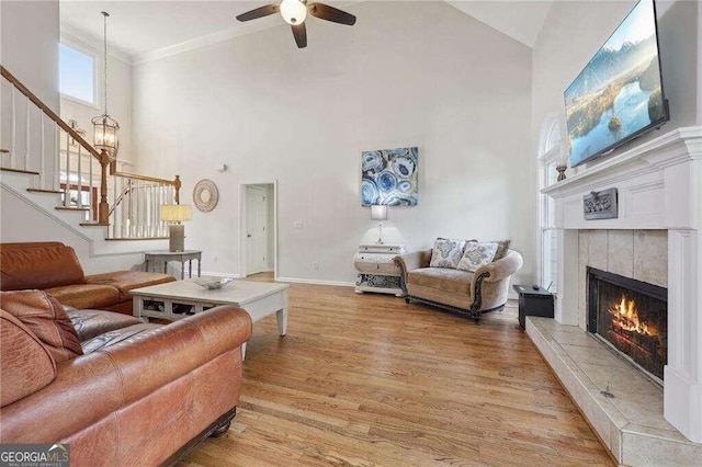 living room featuring ceiling fan, a high ceiling, light hardwood / wood-style floors, a fireplace, and ornamental molding