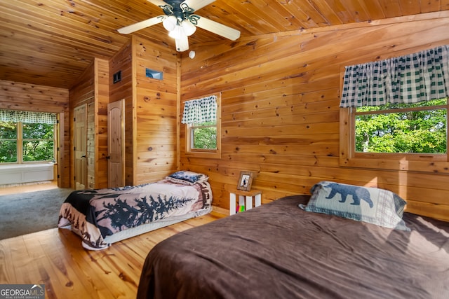 bedroom featuring wood walls, lofted ceiling, multiple windows, and ceiling fan