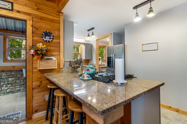 kitchen with stainless steel appliances, kitchen peninsula, a kitchen breakfast bar, light tile patterned floors, and pendant lighting