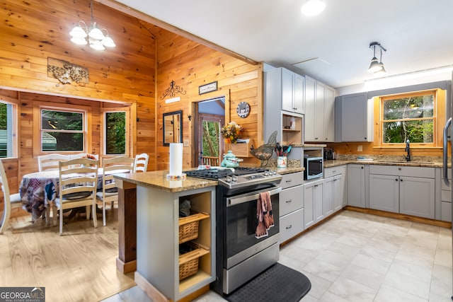 kitchen featuring a wealth of natural light, wood walls, appliances with stainless steel finishes, and hanging light fixtures