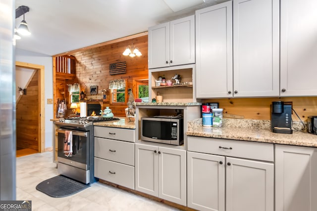 kitchen featuring stainless steel appliances, wood walls, white cabinetry, light stone countertops, and hanging light fixtures