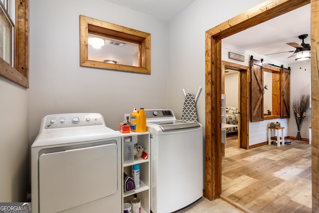 laundry room featuring light wood-type flooring, washing machine and dryer, a barn door, and ceiling fan