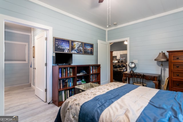 bedroom featuring light wood-type flooring, wood walls, ceiling fan, and stainless steel refrigerator