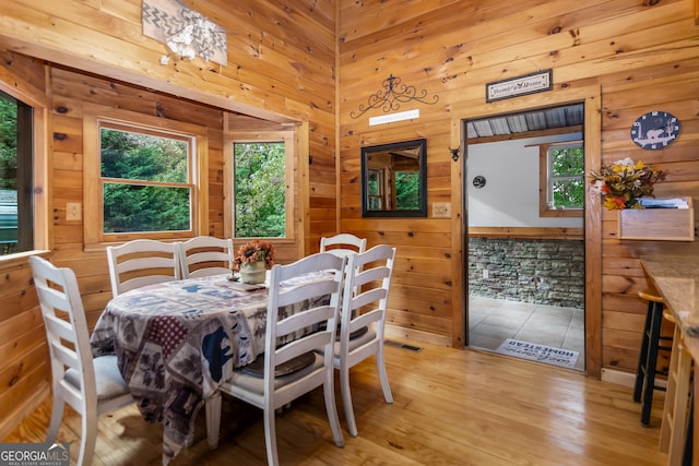 dining space with wood walls, a healthy amount of sunlight, and light hardwood / wood-style flooring