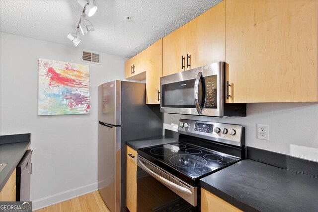 kitchen with a textured ceiling, track lighting, stainless steel appliances, and light hardwood / wood-style floors