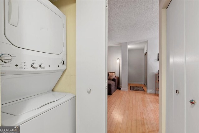 laundry room featuring light hardwood / wood-style floors, a textured ceiling, and stacked washer and dryer