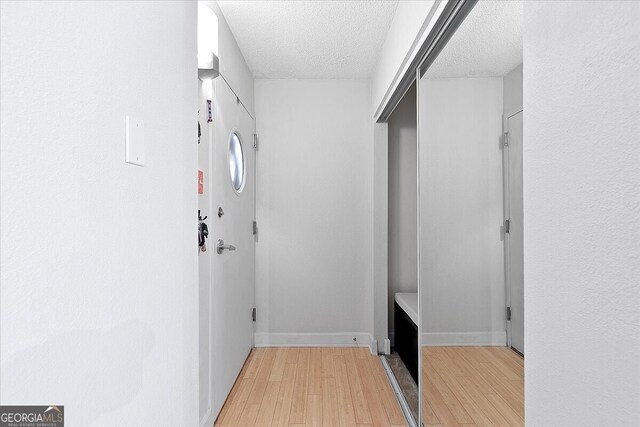 hallway with a textured ceiling and light hardwood / wood-style flooring