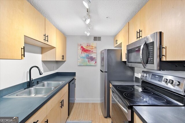 kitchen featuring a textured ceiling, sink, light wood-type flooring, appliances with stainless steel finishes, and light brown cabinetry