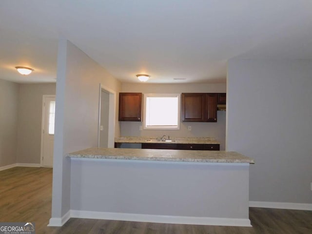 kitchen with light stone countertops, kitchen peninsula, sink, and dark hardwood / wood-style floors