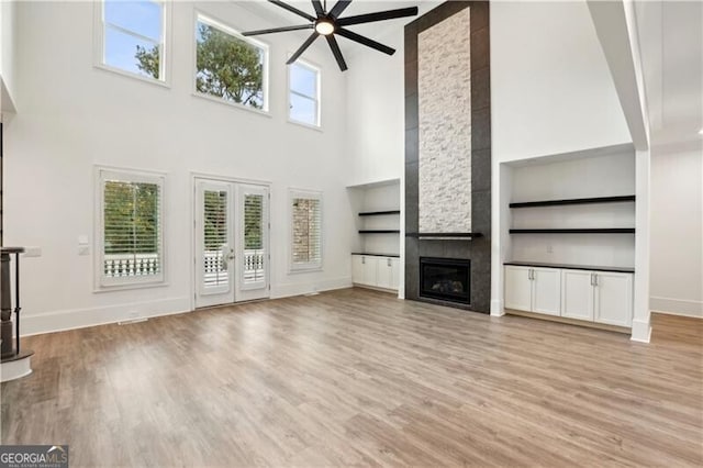 unfurnished living room featuring a fireplace, light wood-type flooring, a towering ceiling, and plenty of natural light