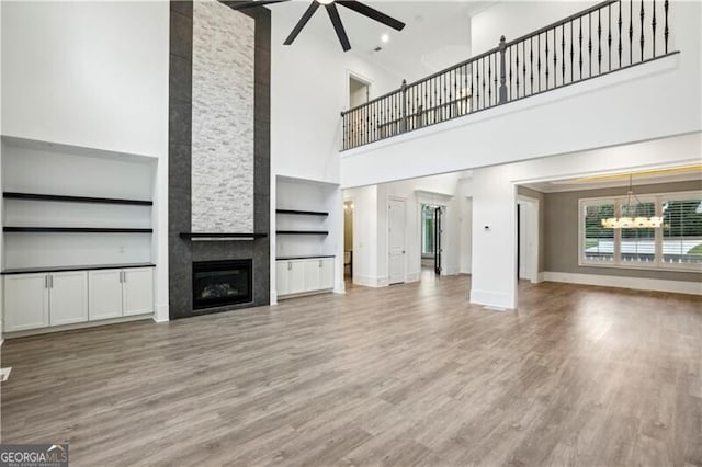 unfurnished living room featuring hardwood / wood-style floors, a towering ceiling, ceiling fan with notable chandelier, and a large fireplace