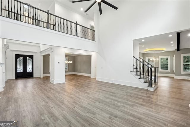 unfurnished living room featuring french doors, a towering ceiling, ceiling fan with notable chandelier, and wood-type flooring