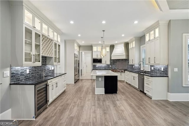 kitchen with stainless steel appliances, a kitchen island, custom range hood, hanging light fixtures, and beverage cooler