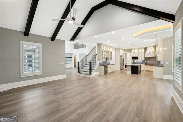 unfurnished living room featuring high vaulted ceiling, ceiling fan with notable chandelier, wood-type flooring, and beamed ceiling